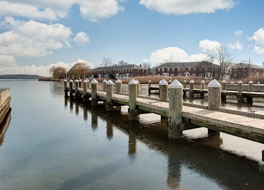 A wooden pier extends into a calm body of water with a building in the background.