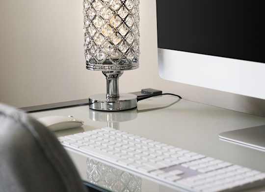 A glass lamp with a diamond pattern stands on a desk next to a computer monitor, keyboard, and mouse.