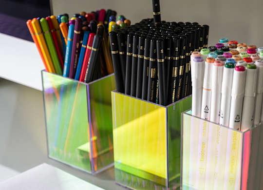 A glass container holds a variety of markers and pens.