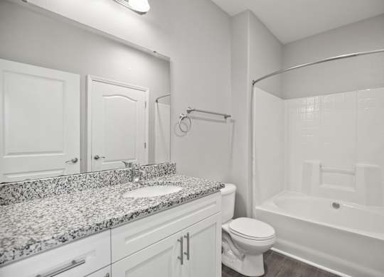 A white bathroom with a granite countertop and a white bathtub.