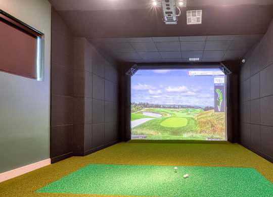 A golf simulator room with a screen showing a golf course.