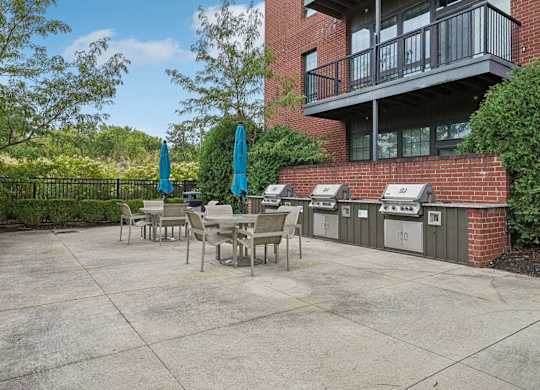 A patio with a table and chairs is surrounded by a brick building and trees.