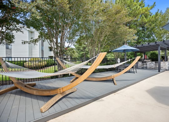 two hammocks on a patio with umbrellas and trees