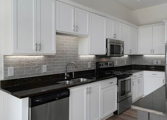 A kitchen with white cabinets and black countertops.