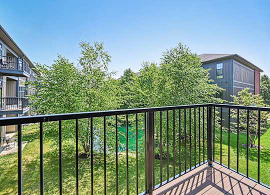 A balcony with a black railing overlooks a green lawn and trees.