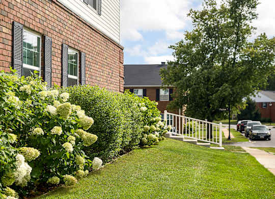 A white fence separates a green lawn from a brick building.