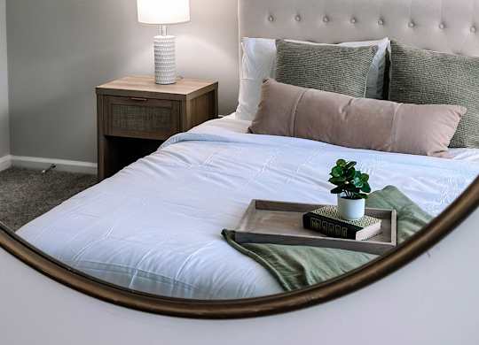 A bedroom with a bed, a nightstand with a lamp, and a painting on the wall.