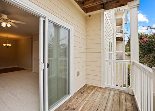 A balcony with a glass door leading to a room with a ceiling fan.
