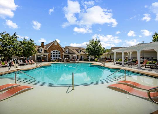 A large swimming pool with lounge chairs and a house in the background.