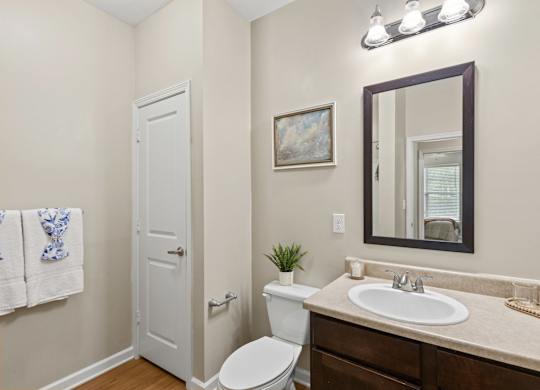 A bathroom with a toilet, sink, mirror, and a door.
