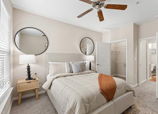 A bedroom with a large bed, a ceiling fan, and two round mirrors on the wall.