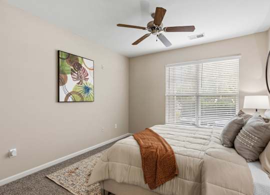 A bedroom with a bed, a ceiling fan, and a painting on the wall.
