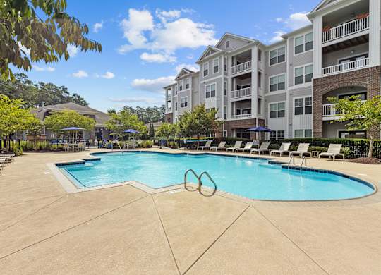 A large swimming pool surrounded by lounge chairs and apartment buildings.