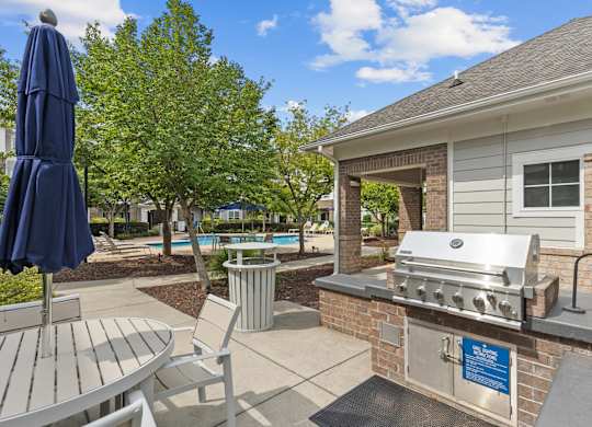 A blue umbrella is on a table next to a grill.