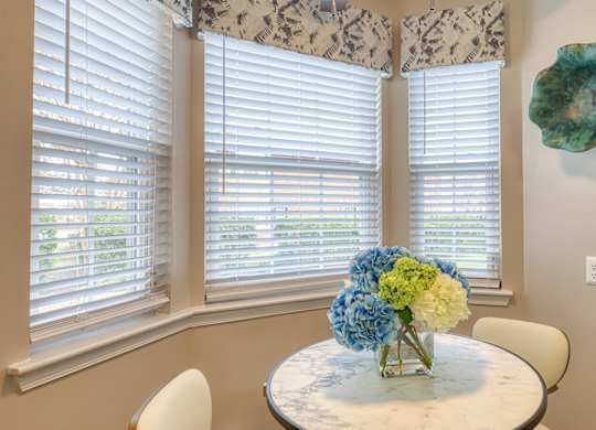 A dining room with a table and chairs and a vase of flowers.