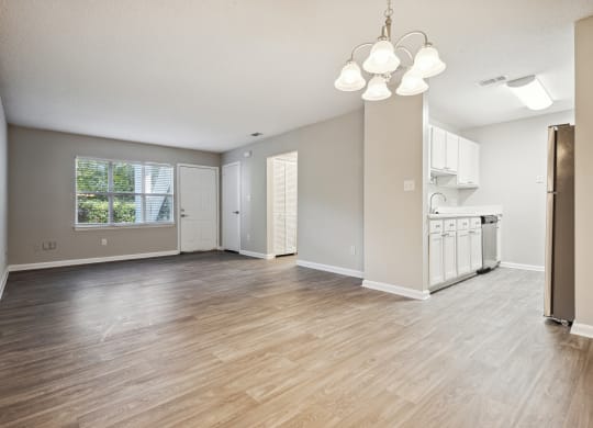 an empty living room with a kitchen in the background