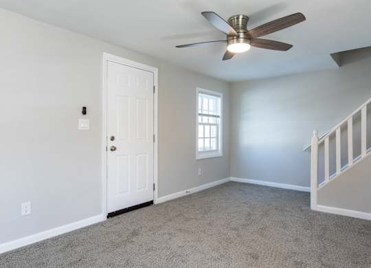 A room with a ceiling fan and a staircase.