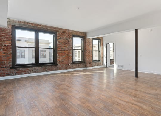 an empty living room with a brick wall and wood floors at The Madison, Columbus