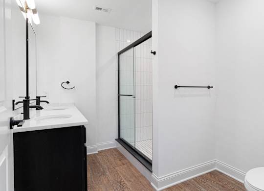 A white bathroom with a black vanity and a walk-in shower.