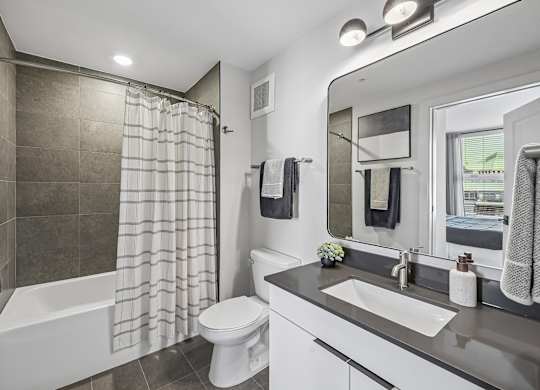 A modern bathroom with a white toilet, a bathtub with a shower curtain, a sink, and a mirror.