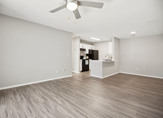 an empty living room with a ceiling fan and a kitchen