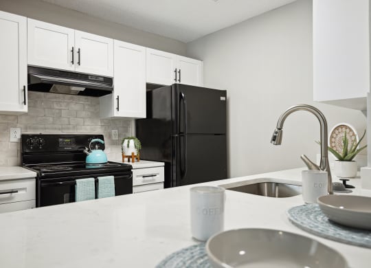 a kitchen with white cabinets and a sink and black refrigerator