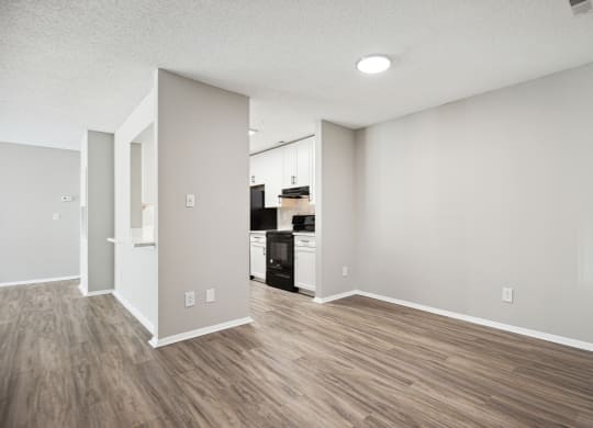 an empty living room and kitchen with white walls and wood flooring