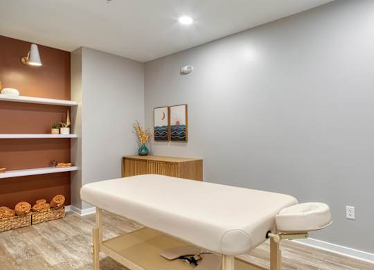 A massage table in a room with a shelf and towels.