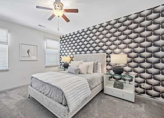A bedroom with a bed, a ceiling fan, and a patterned wallpaper.