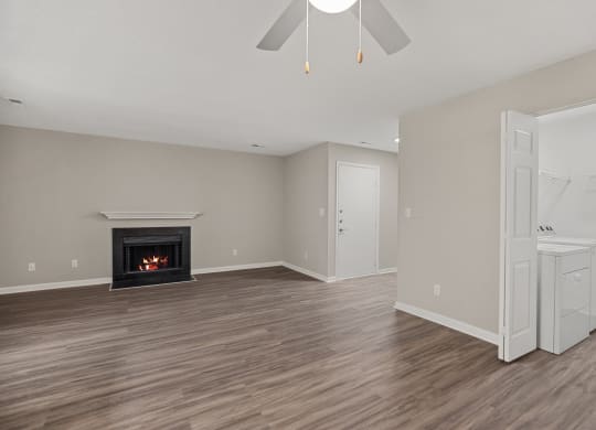 an empty living room with a fireplace and a white kitchen