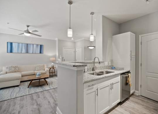 A modern kitchen with a white color scheme and a living room area with a sofa and a table.