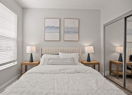 A bedroom with a large bed, two lamps, and two framed pictures on the wall.