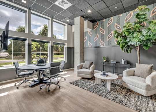A modern living room with a grey couch, a white coffee table, and a large window with a view of trees.