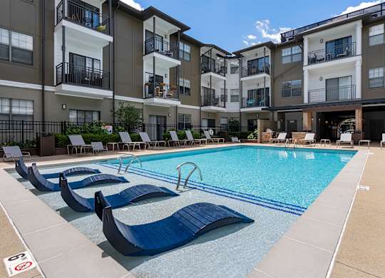 A swimming pool with lounge chairs in front of apartment buildings.