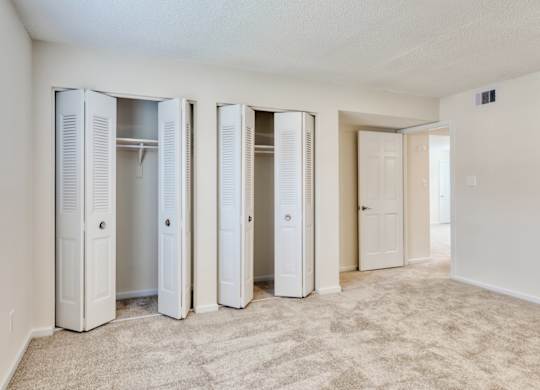 A room with white walls and a carpeted floor with four white closets.