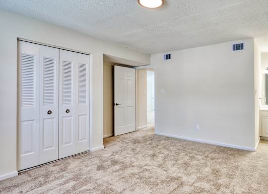 A room with white walls, a carpeted floor, and a small window with blinds.