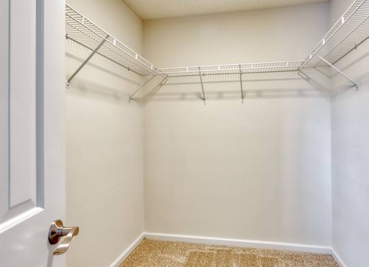 A white door is on the left of a room with a carpeted floor and a metal shelf above.