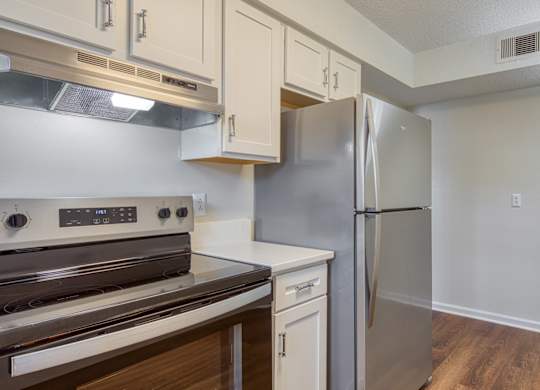 A kitchen with a stove top oven, refrigerator, and wooden floors.