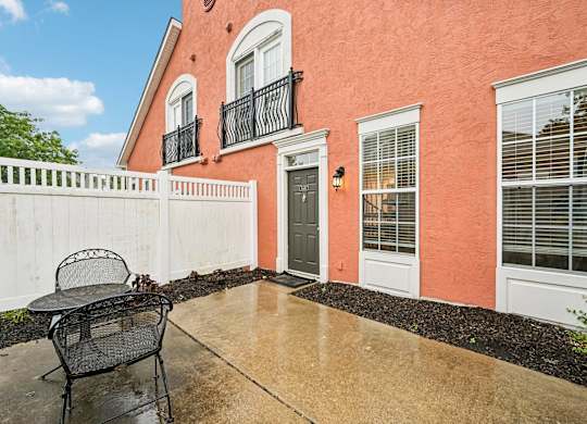 A patio with a chair and a table is in front of a house.
