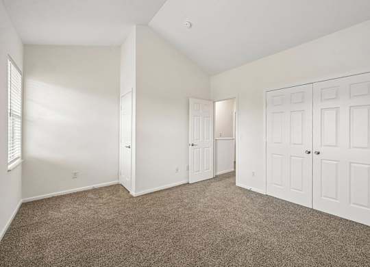 A room with white walls and carpeted floor with a door on the right.
