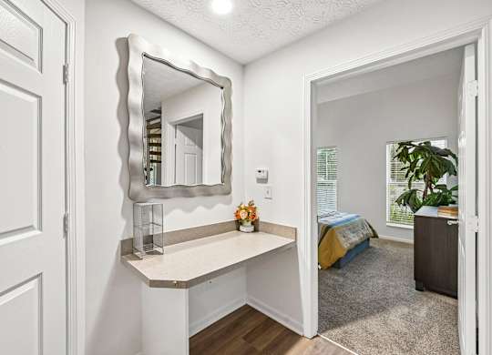 A white door is on the left of a room with a mirror and a bed in the background.