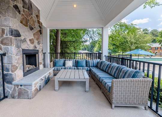 A patio with a stone fireplace and a wicker sofa.