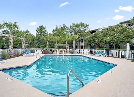 A large swimming pool surrounded by palm trees and lounge chairs at Litchfield Oaks Apartments in Pawleys Island, 29585