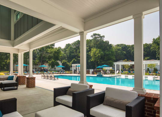 a covered patio with couches and chairs and a pool in the background
