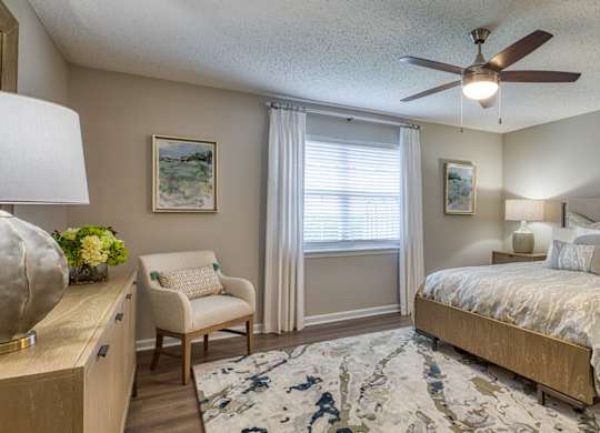 A bedroom with a bed, chair, and a ceiling fan.