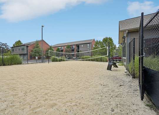 A sandy volleyball court with a net and a fence.