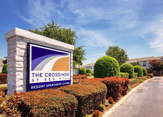 A sign for The Crossings at Red Mill Resort Apartment Living stands in front of a row of bushes.