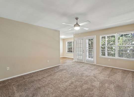 A room with a carpeted floor, a ceiling fan, and a window with blinds.