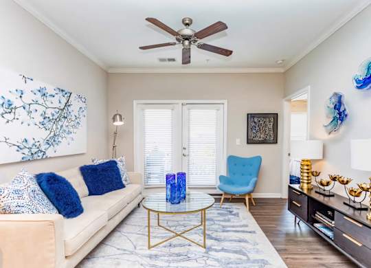 A living room with a beige couch, a blue chair, and a painting on the wall.