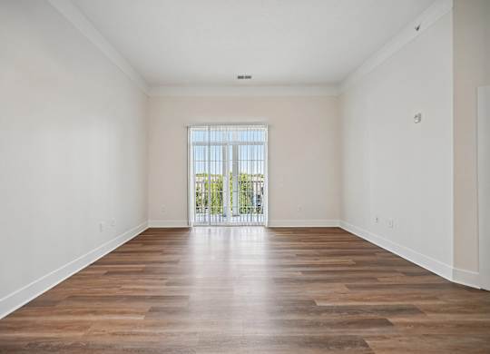 A room with wooden floors and a window with a view of a balcony.